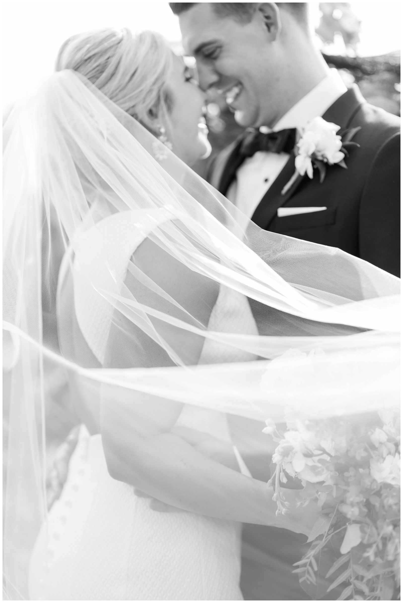 black and white portrait of the bride and groom touching noses with veil around shoulders