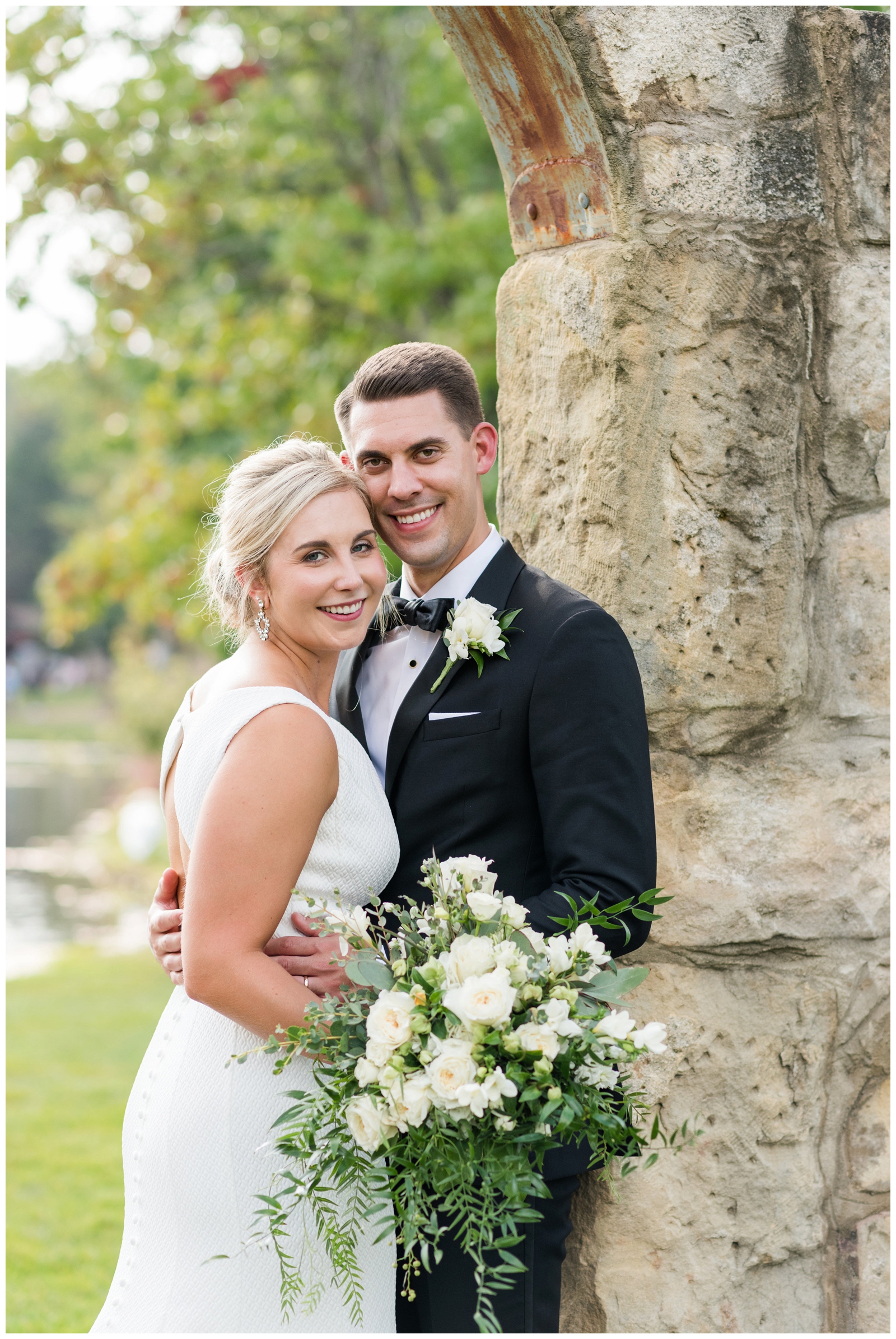 groom in tux with white boutonnière and bride with all-white bouquet hug at Gervasi Vineyard