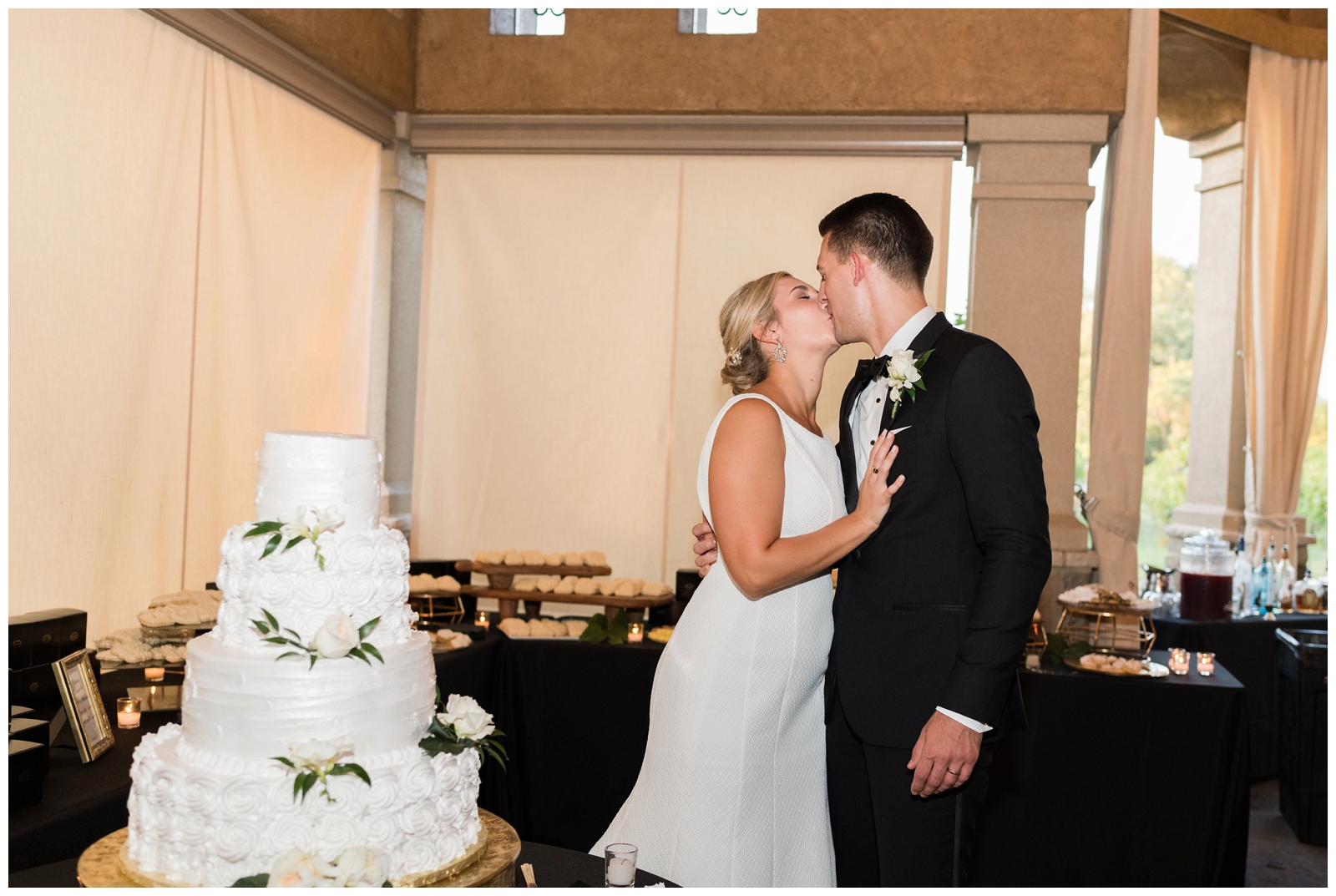 bride and groom kiss by four tiered wedding cake at Gervasi Vineyard