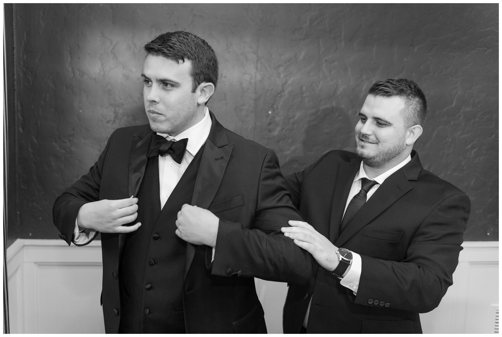 groomsman helps groom into tux jacket before Brookside Golf and Country Club wedding