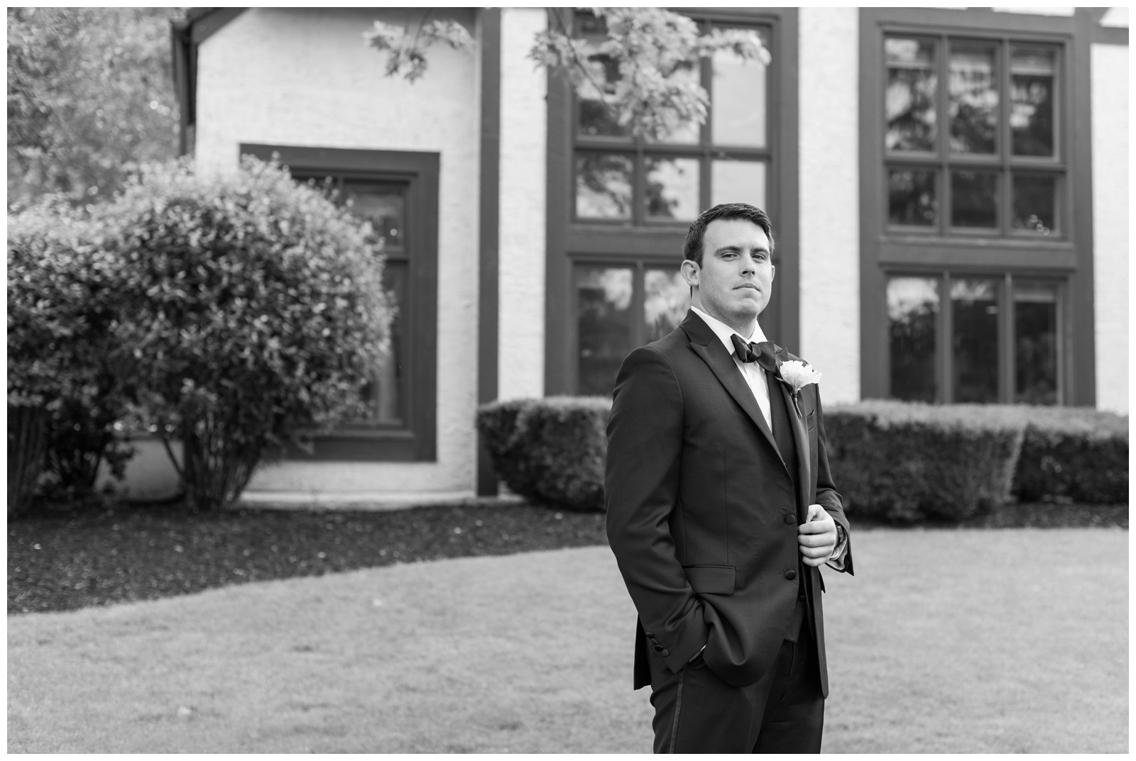 black and white portrait of groom in suit and flower boutonnière outside Brookside Golf and Country Club 