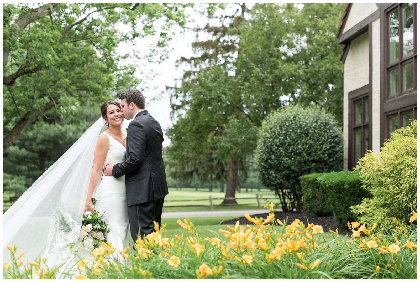 groom kisses bride in gardens at Brookside Golf and Country Club by yellow flowers