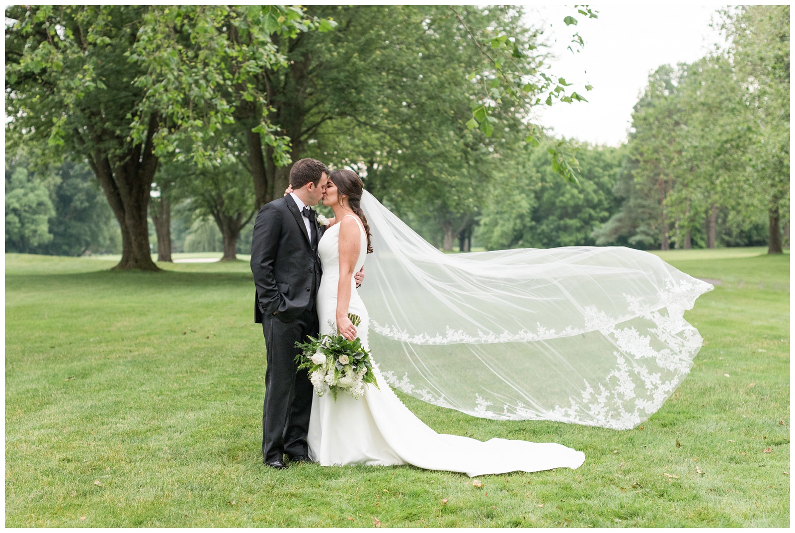bride and groom kiss while bride's lace veil floats in the wind
