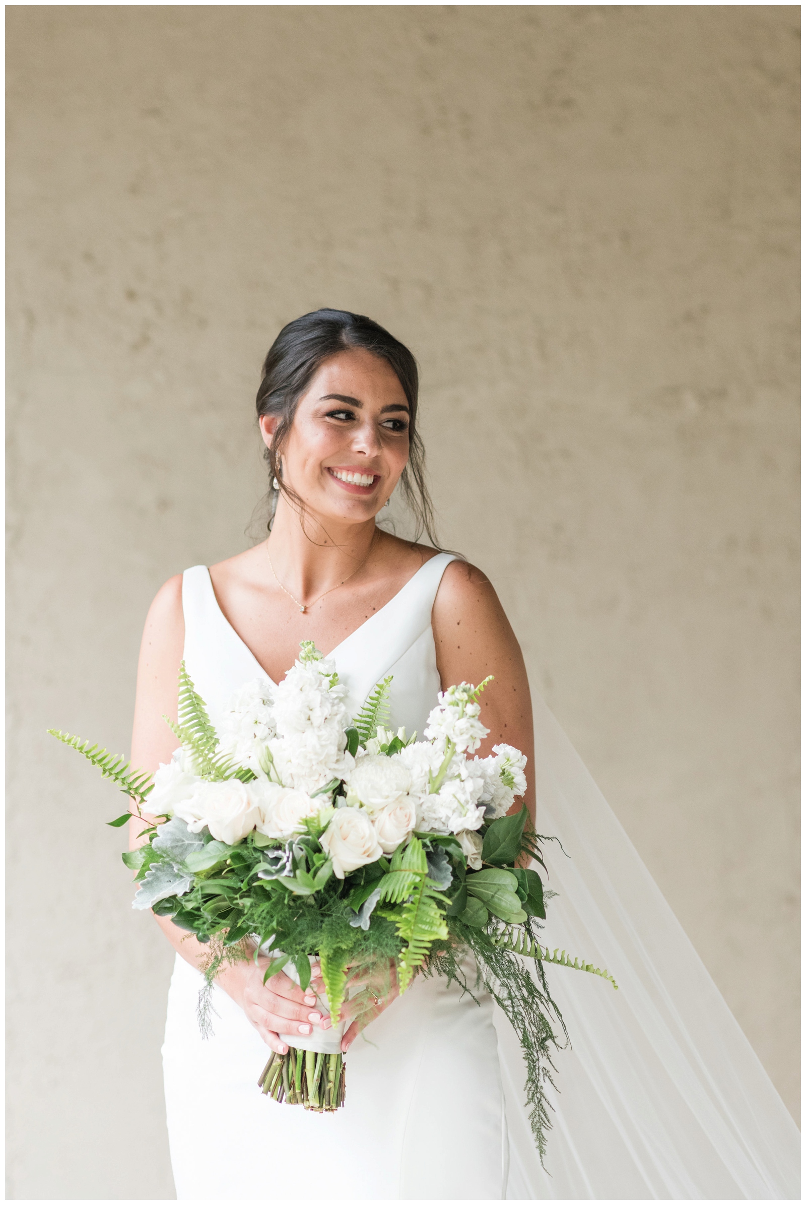 bridal portrait against tan wall while bride holds white bouquet with pale pink flowers at Brookside Golf and Country Club 