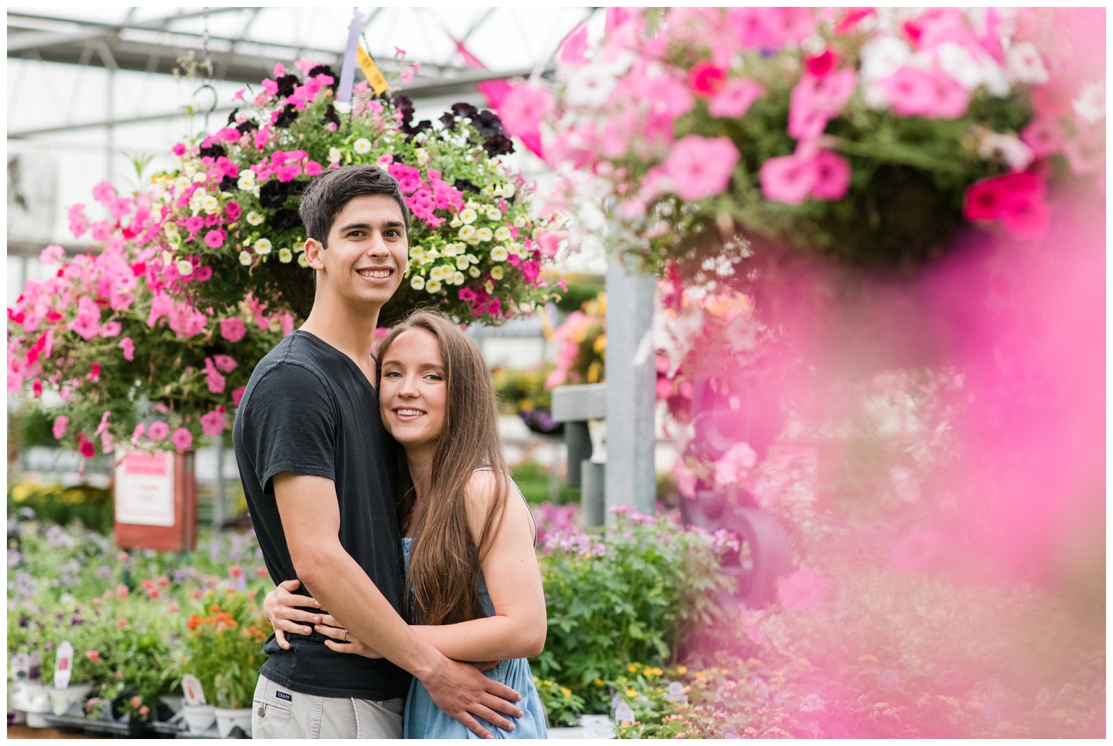 bride and groom pose by bright pink flowers in local Ohio nursery for greenhouse inspired engagement session