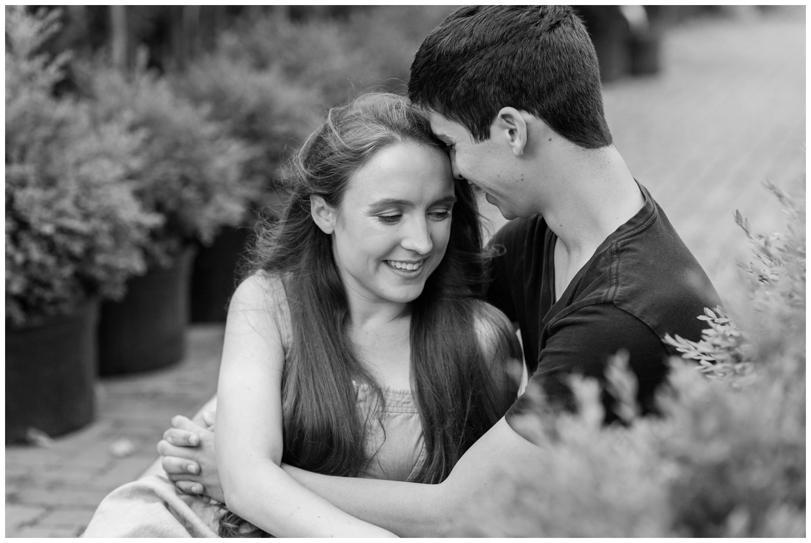 couple snuggles together by plants in Oakland Nursery during New Albany Ohio engagement session