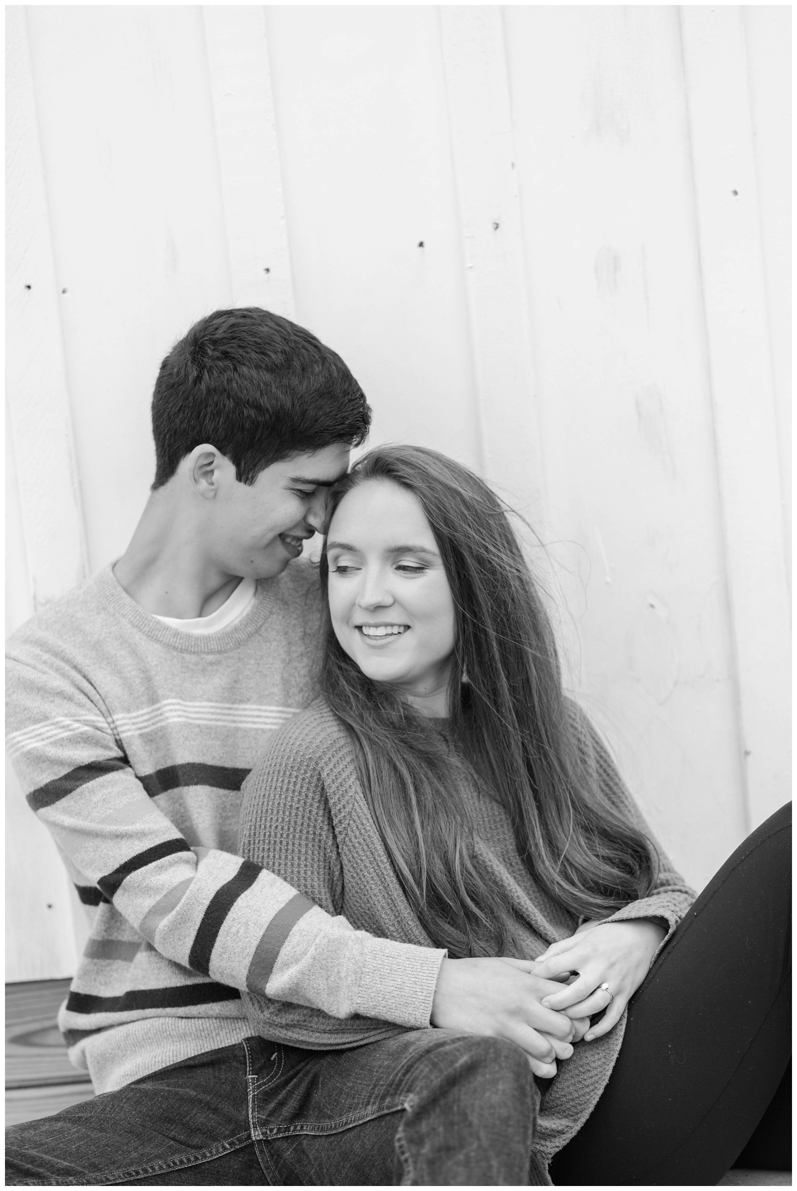 black and white portrait of engaged couple in cozy sweaters by wood paneled wall