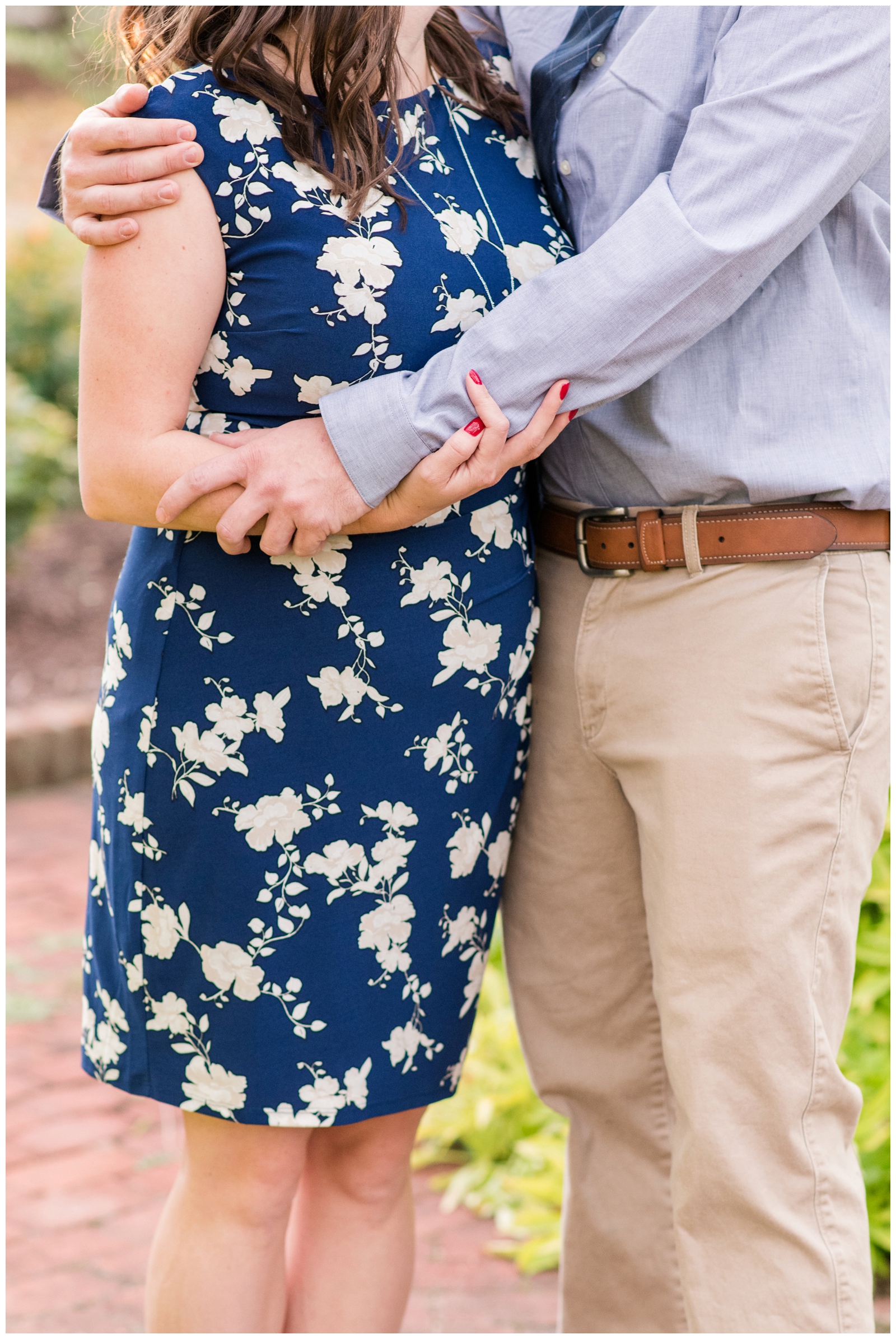 bride holds onto groom's arm with red painted nails in blue dress with white flowers