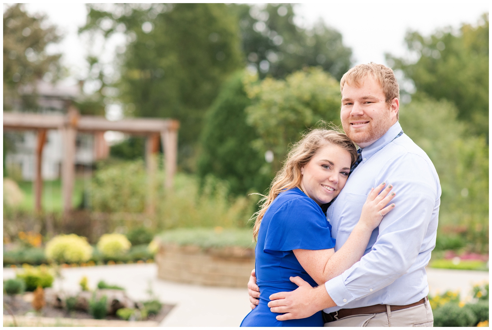 bride in bright blue shirt hugs groom during summer engagement session Dawes Arboretum