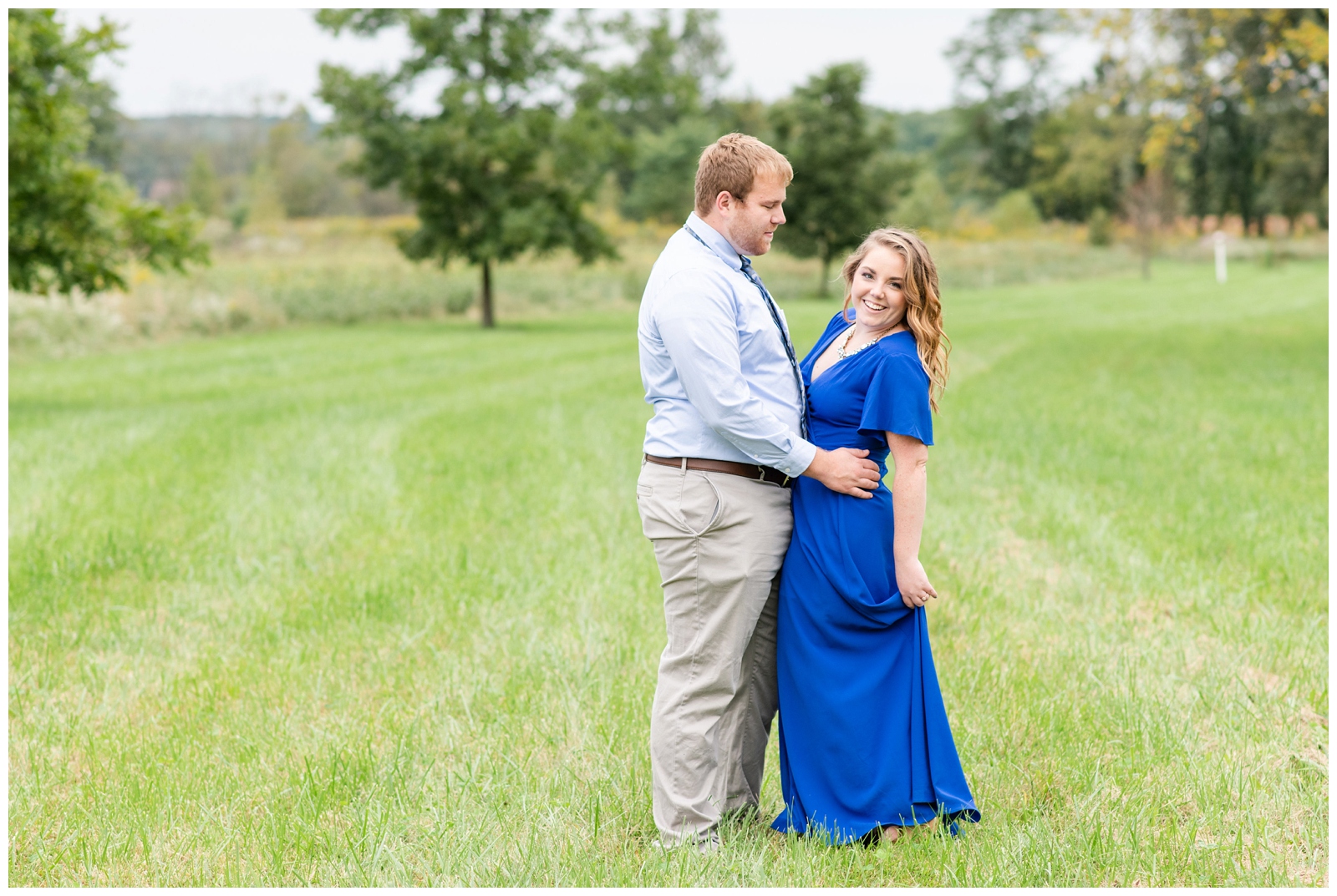 newly engaged couple dances in the grass during summer engagement session Dawes Arboretum