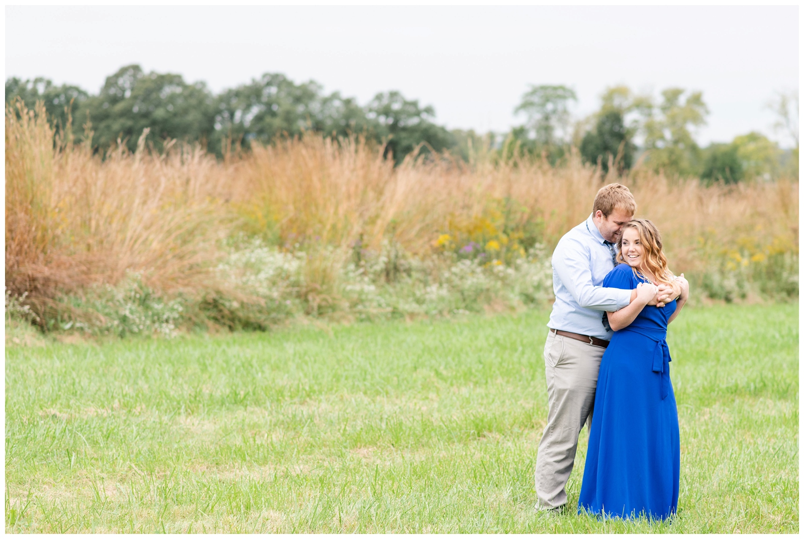 groom hugs bride from behind next to field of tall grass at Dawes Arboretum 