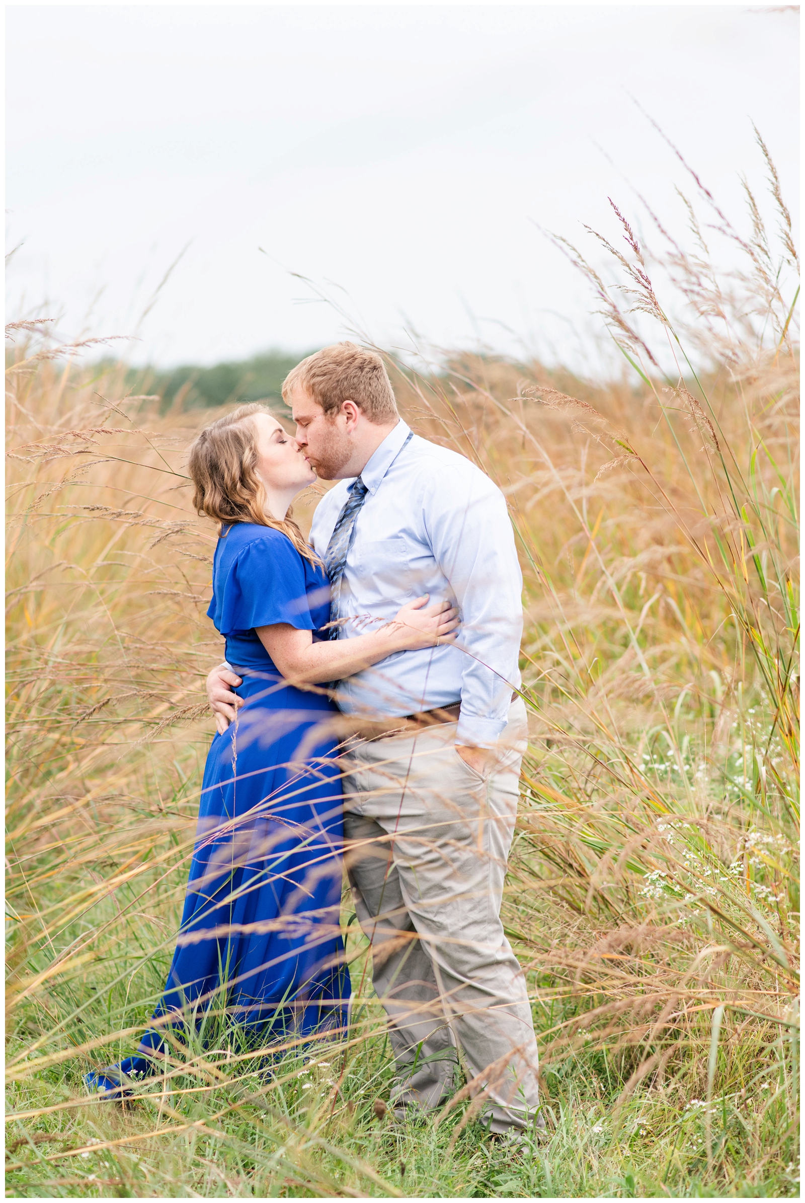 engaged couple kisses in field with tall grass at summer engagement session Dawes Arboretum
