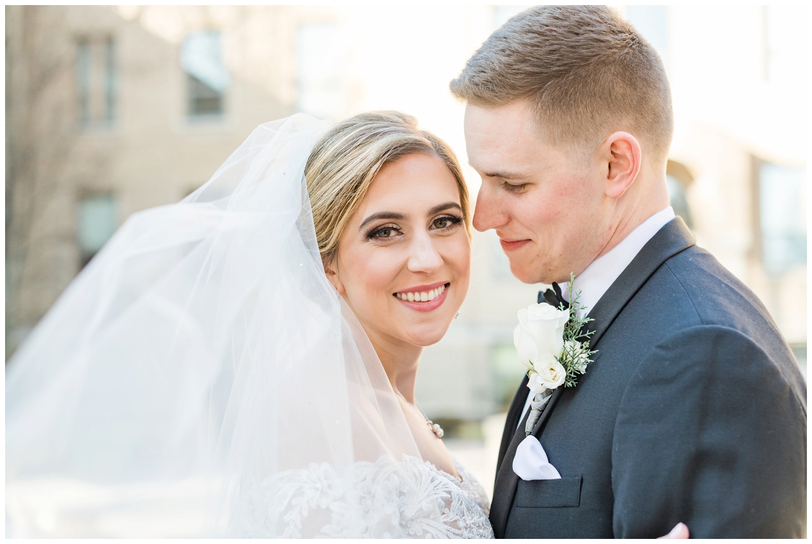 bride looks at photographer while groom looks at her during Christmas wedding portraits at St. Charles Preparatory School