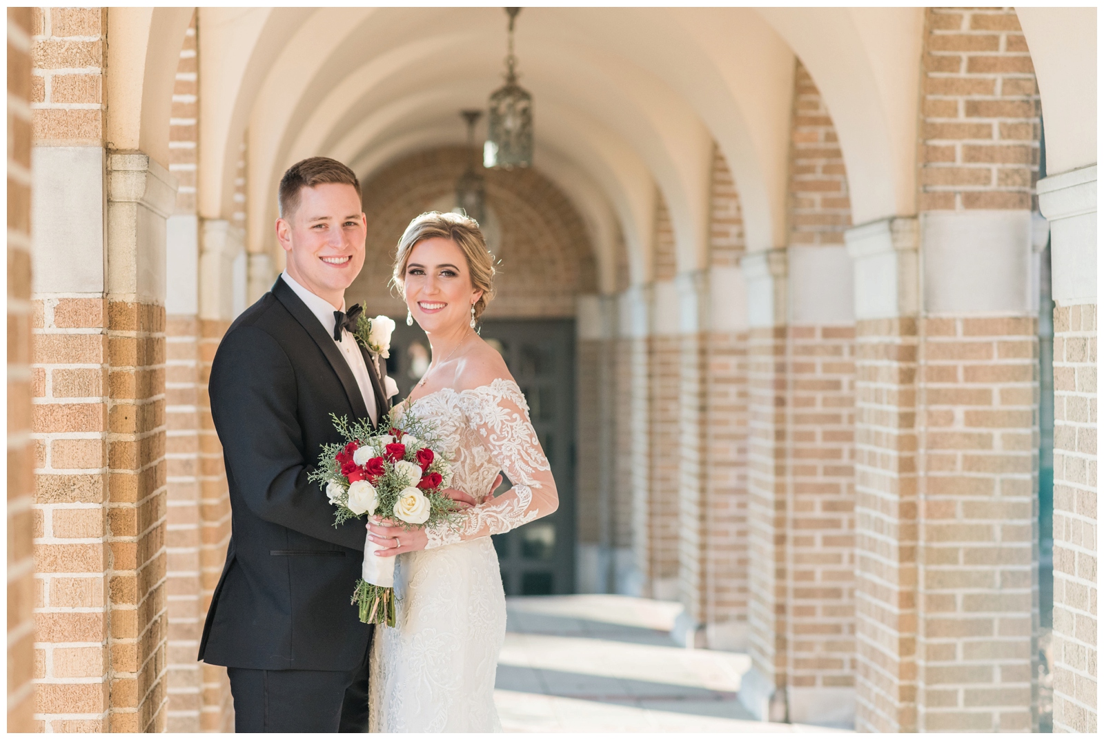 bride and groom hold red and white rose bouquet in brick walkway at St. Charles Preparatory School