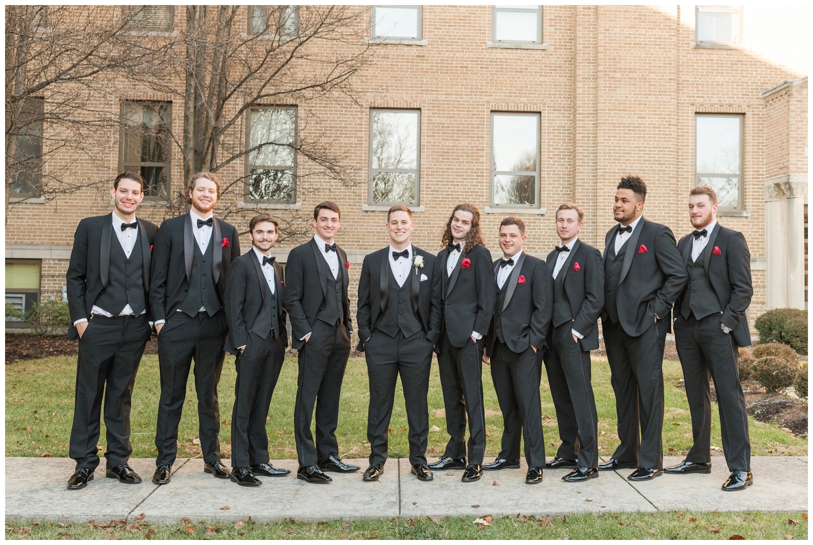 groom stands with nine groomsmen in black suits with red boutineeres