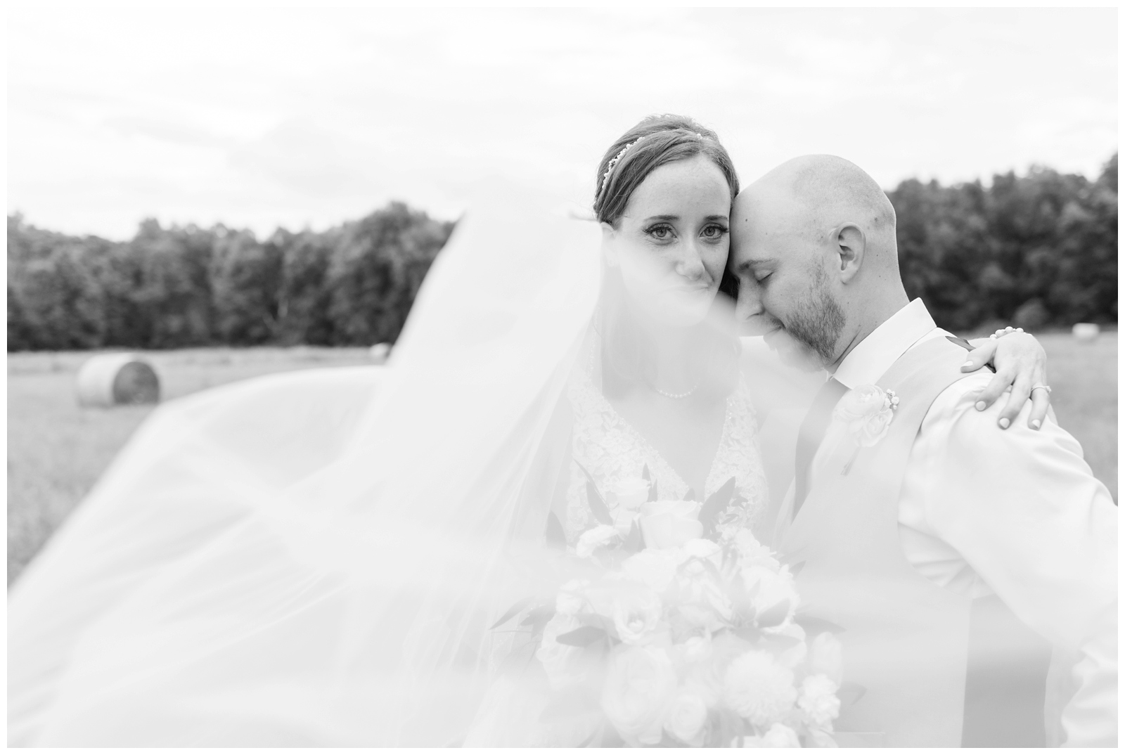 black and white portrait of groom leaning against bride while veil floats