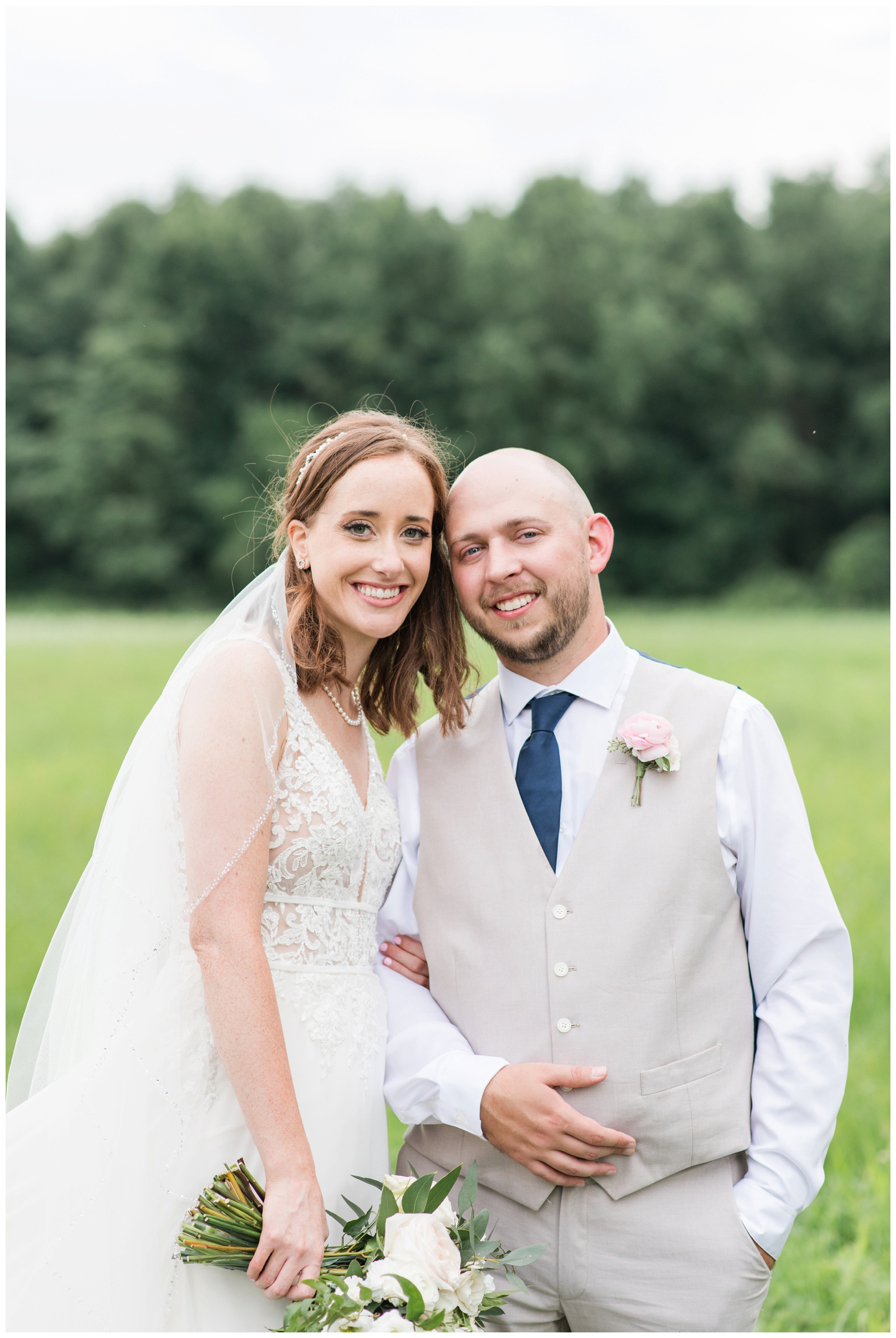bride and groom stand cheek to cheek during summer wedding portraits in field