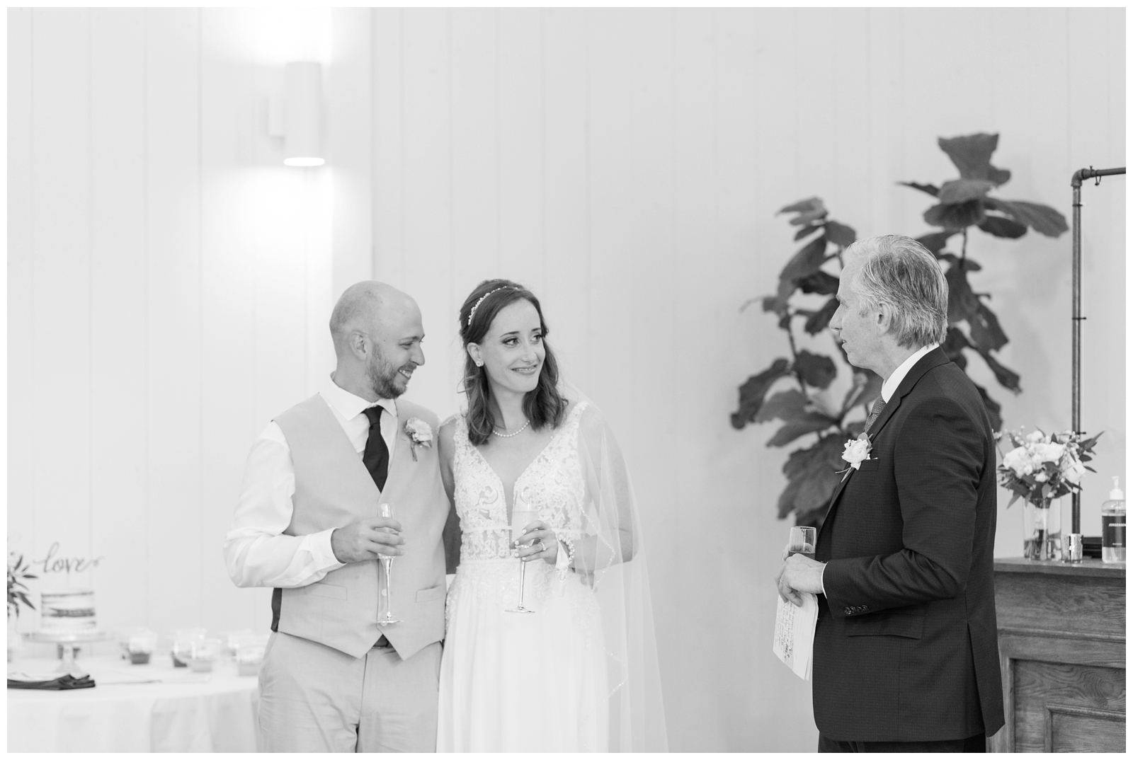 father of the bride gives toast while newlyweds look at him