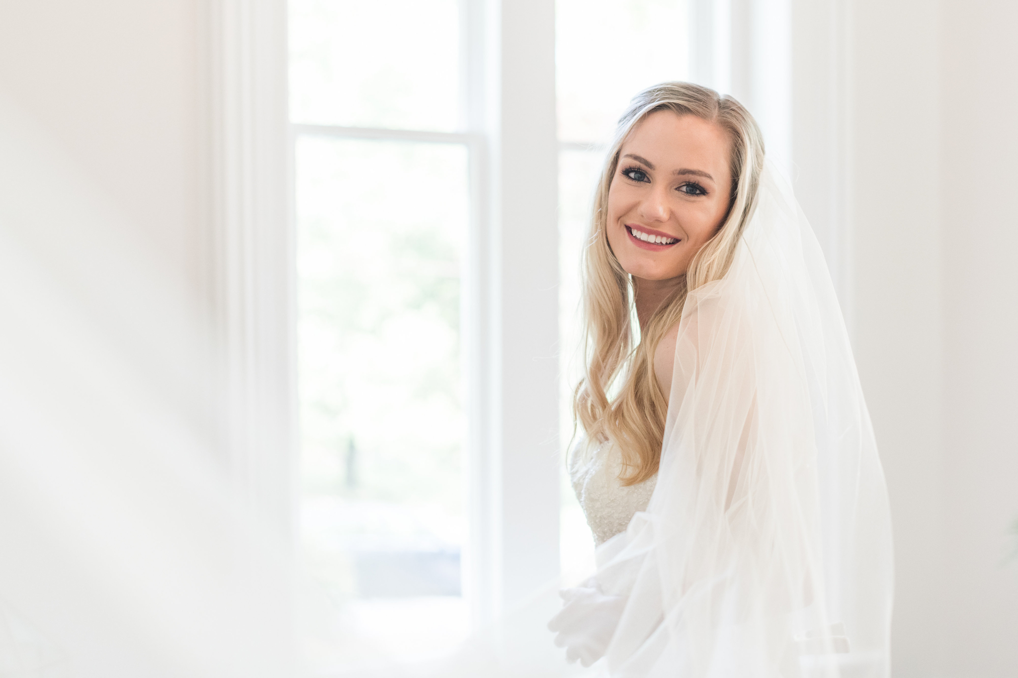 A happy Magnolia Hill Farm bride smiles over her shoulder in the getting ready room in her veil
