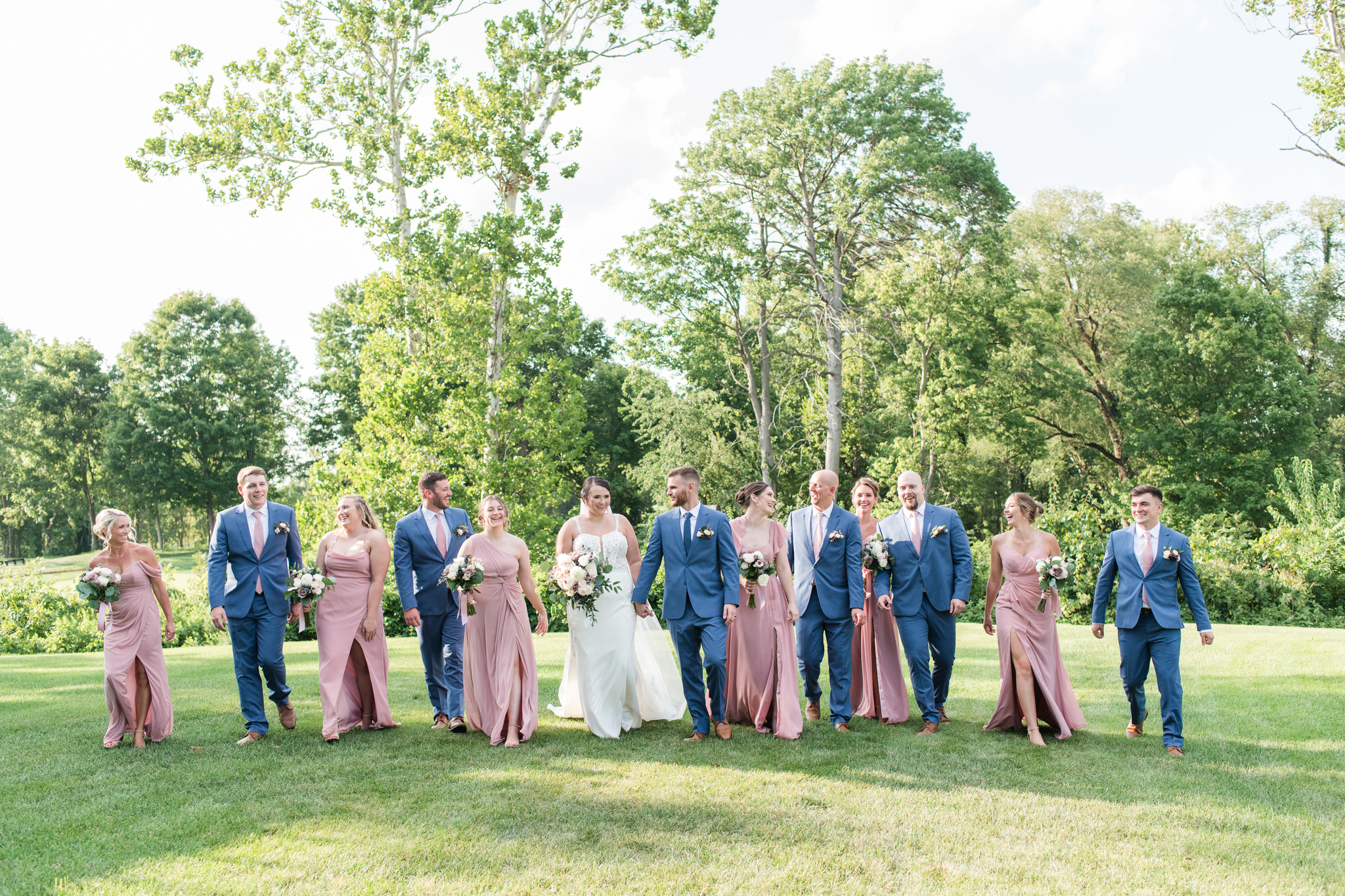 A bride and groom walk smiling with their wedding party in pink and blue in the lawn