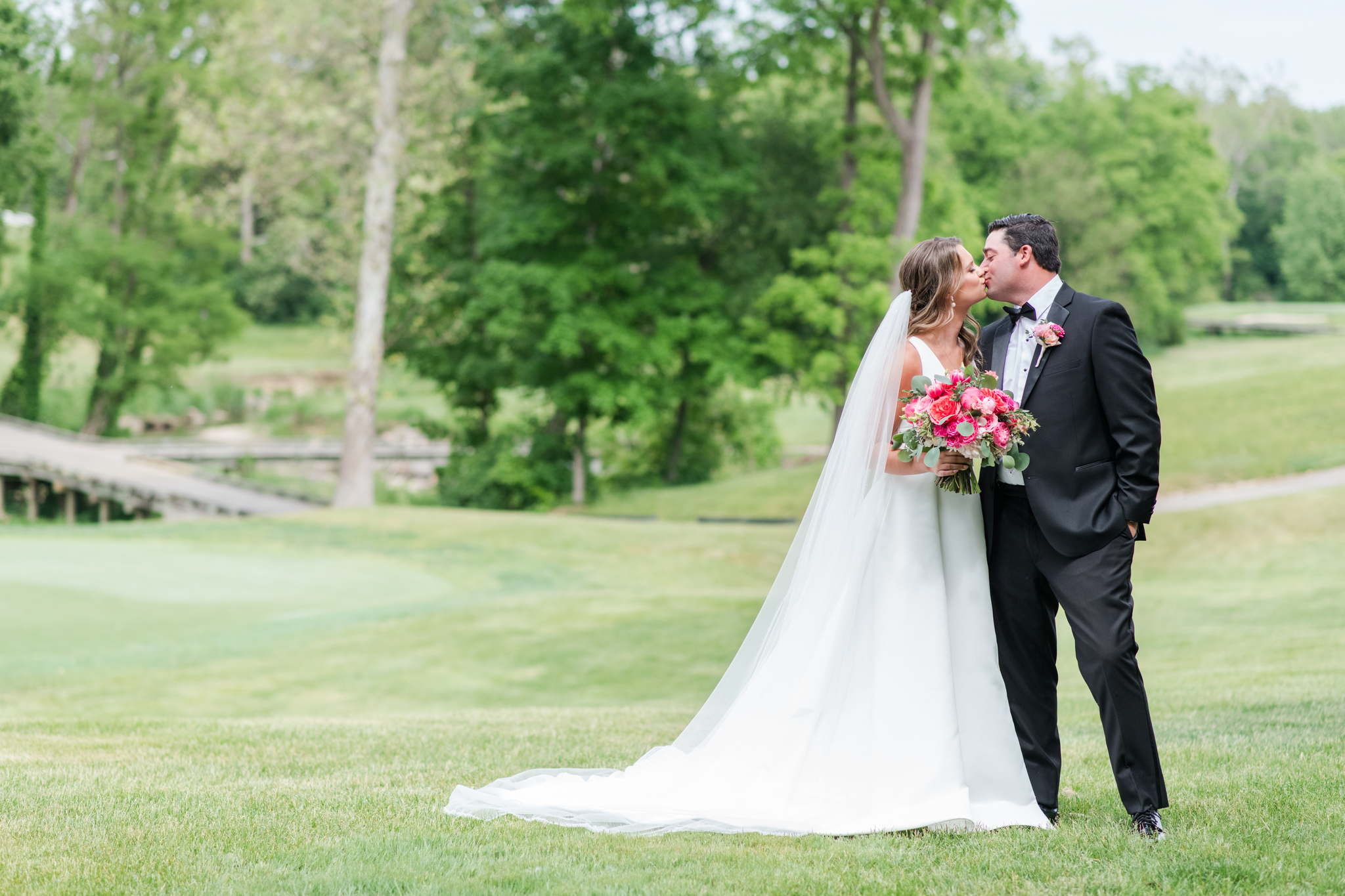 Newlyweds kiss in the lush lawn of their venue with pink bouquet