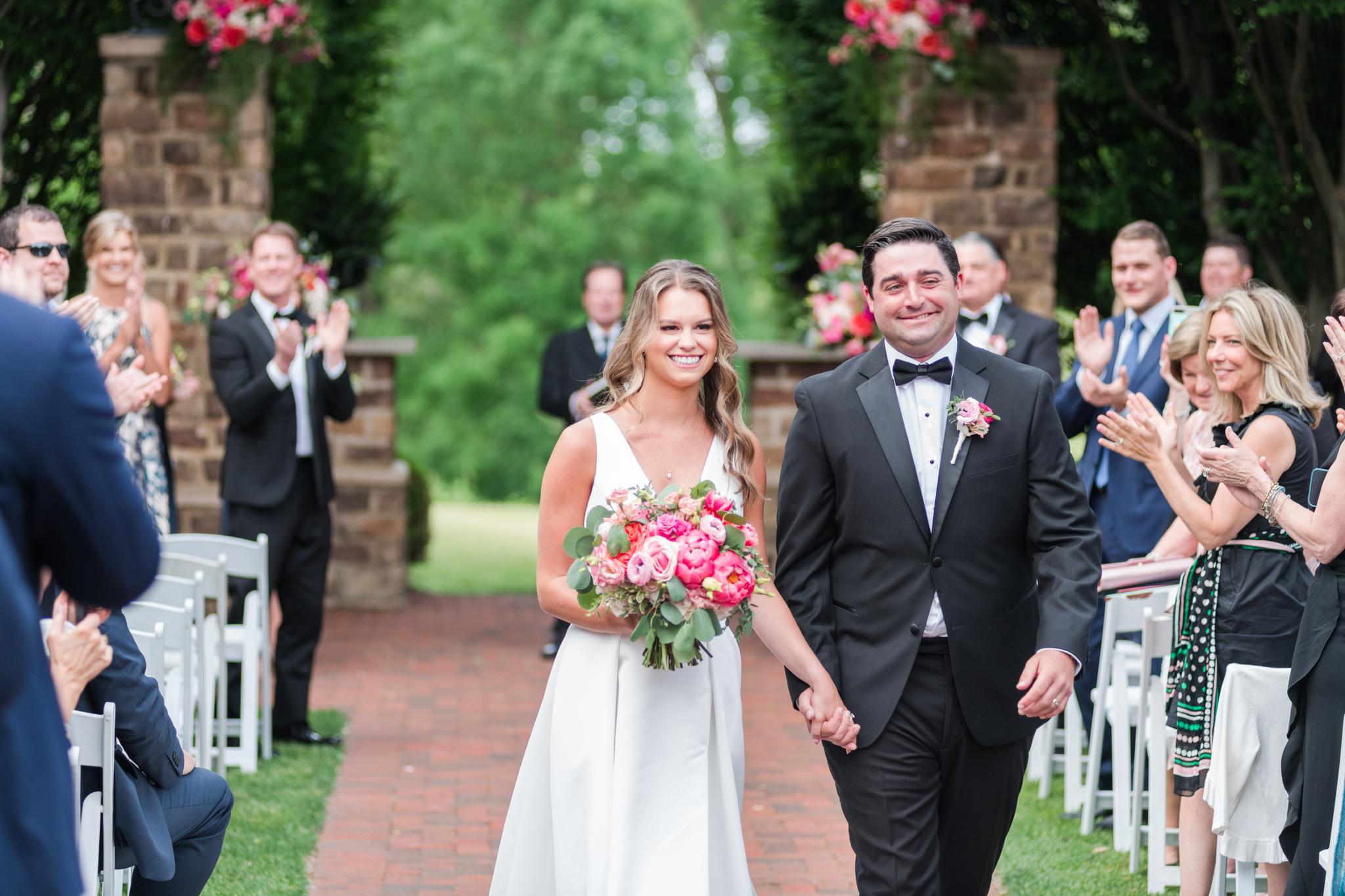 Newlyweds smile big while walking up the aisle holding hands to applause from guests