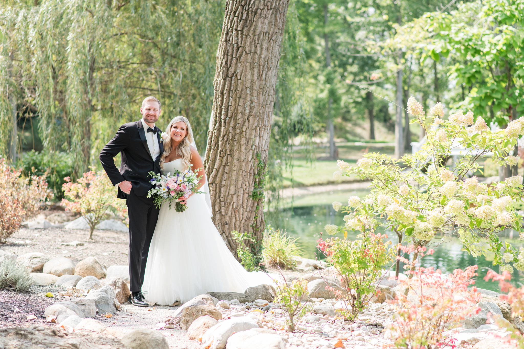 Newlyweds smile while exploring the lakeside gardens of the Swan Lake Event Center