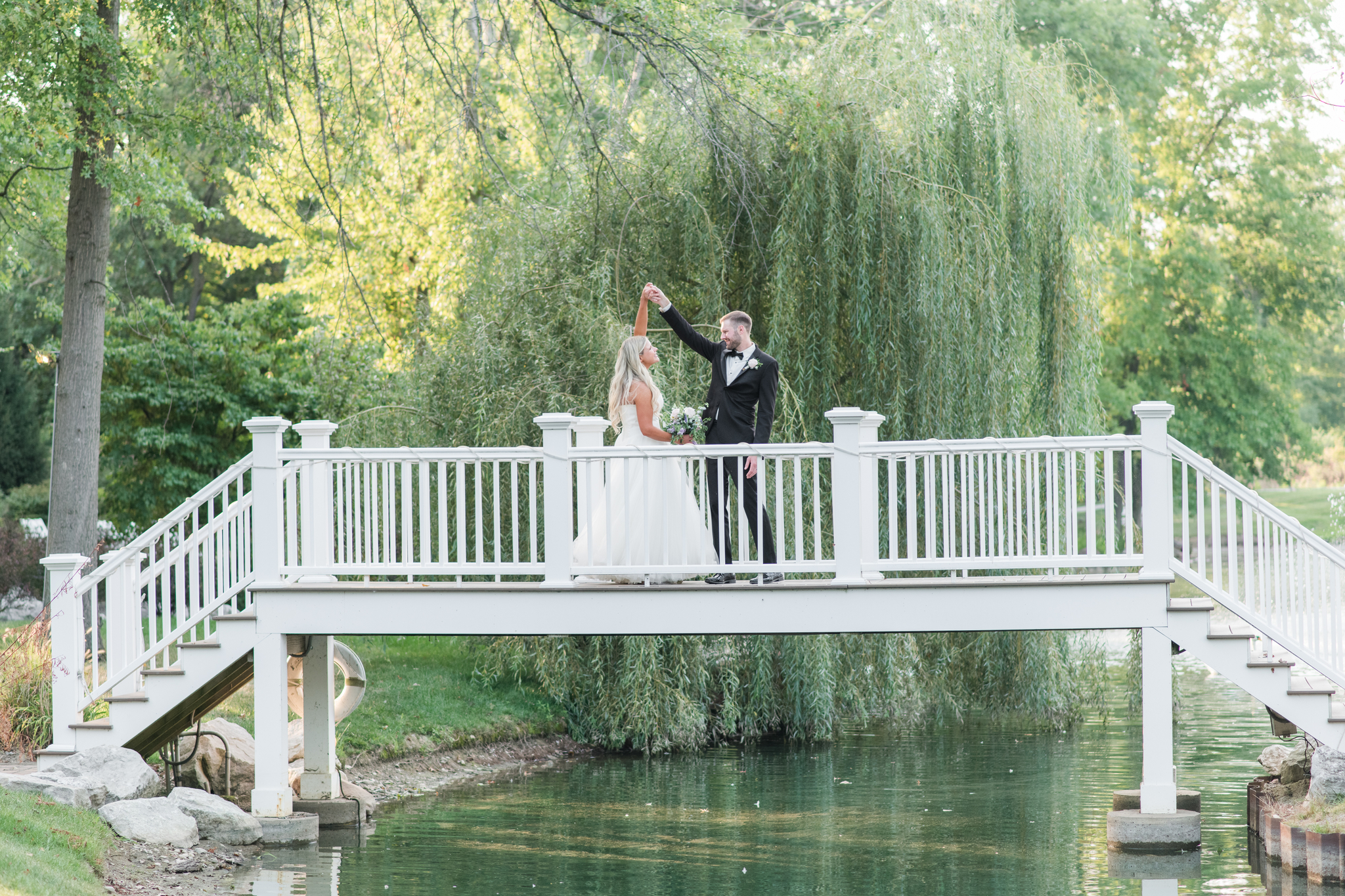 Newlyweds dance on a white bridge over a stream at their Swan Lake Event Center wedding