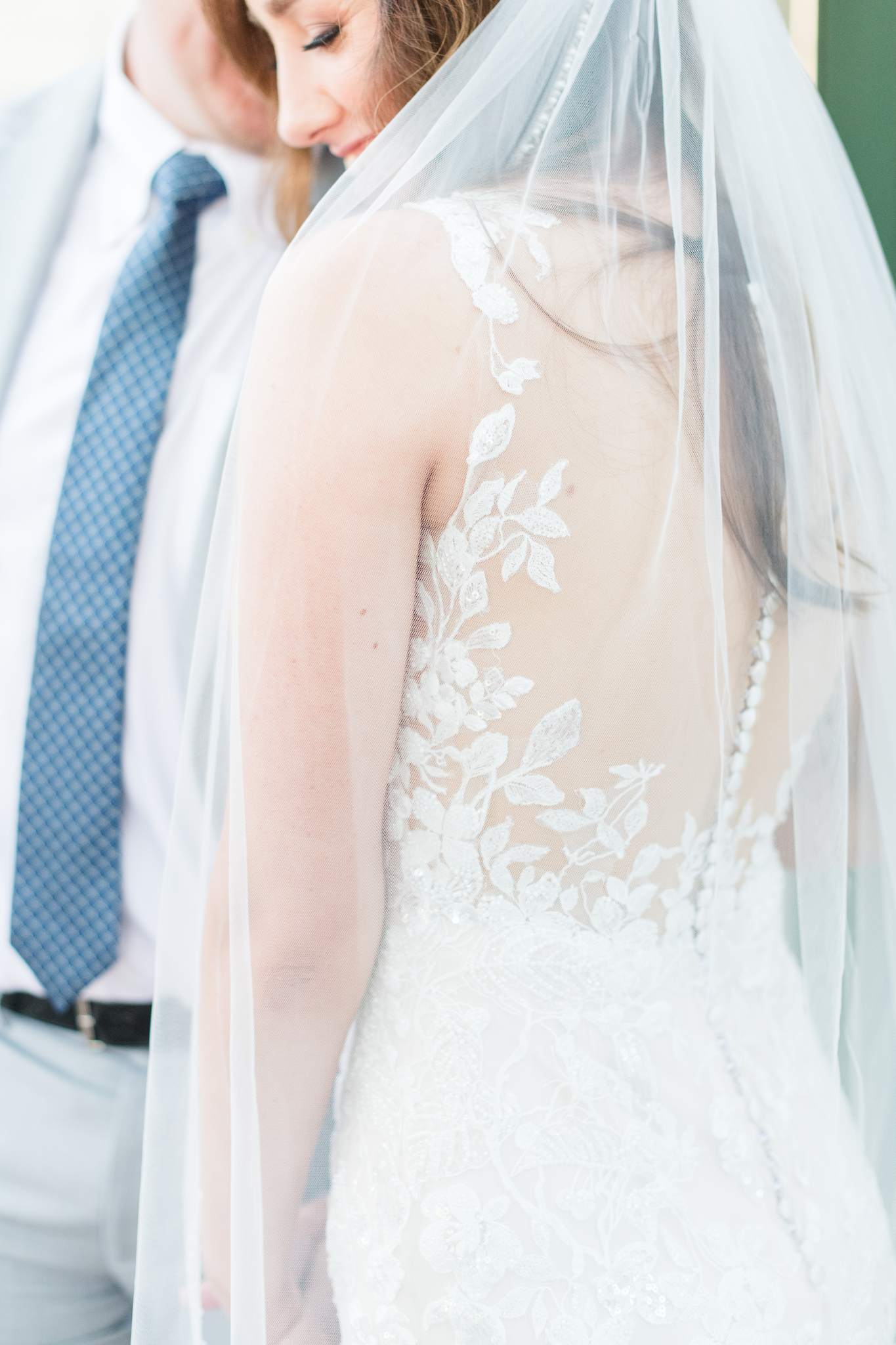 A bride giggles down her shoulder in a floral lace dress with long veil