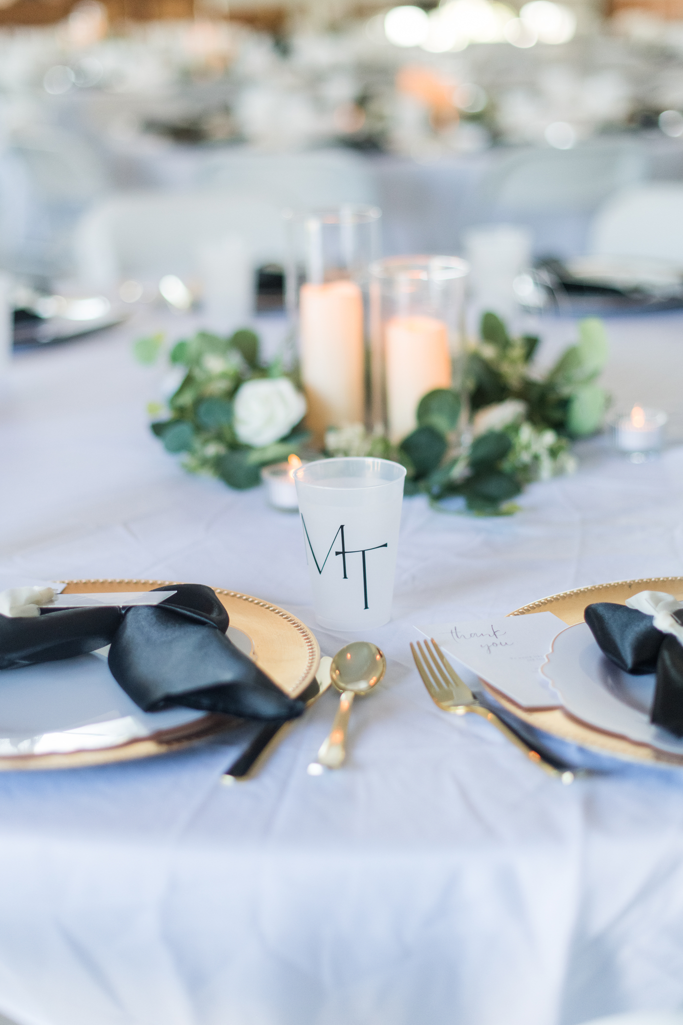 Details of a White Rose Barn wedding reception table set up with a shot glass and gold utensils and candles